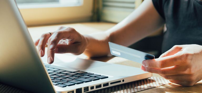 Gros plan d'une personne passant une commande en ligne, on voit l'ordinateur les deux mains et une carte bleue