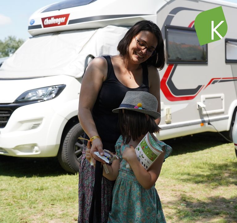 Une maman et son enfant recevant un beignet pasquier devant un camping car