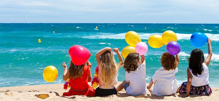 Cinq fillettes de dos sur la plage avec des ballons dans les mains, avec la mer en fond